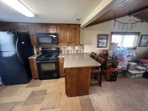 Kitchen featuring a peninsula, a kitchen breakfast bar, light countertops, brown cabinets, and black appliances