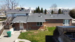 Rear view of property with brick siding, fence, a yard, roof with shingles, and a chimney