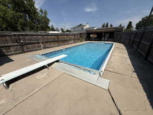 View of swimming pool featuring a diving board, a patio area, and a fenced backyard