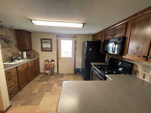 Kitchen with tasteful backsplash, a sink, a textured ceiling, and black appliances