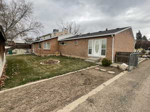 Back of property with entry steps, central AC unit, a fenced backyard, brick siding, and a lawn