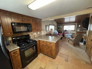 Kitchen featuring a peninsula, visible vents, open floor plan, light countertops, and black appliances