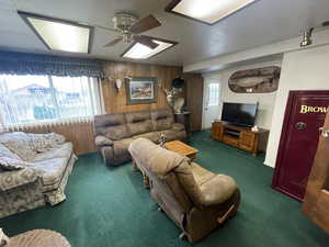 Living room with wood walls, carpet flooring, and a ceiling fan