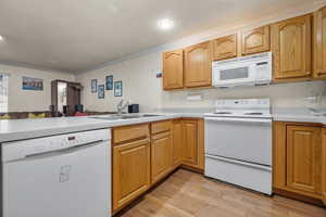 Kitchen with crown molding, light wood-style floors, a sink, white appliances, and a peninsula