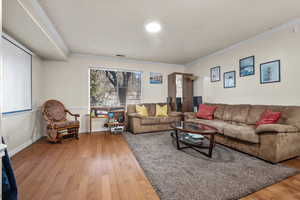 Living area with baseboards, wood-type flooring, visible vents, and crown molding