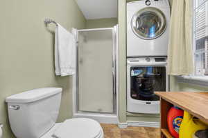 Full bathroom with stacked washer / dryer, a shower stall, and toilet