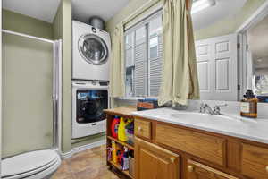 Bathroom featuring a stall shower, stacked washer / dryer, tile patterned flooring, and vanity