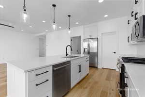 Kitchen with hanging light fixtures, appliances with stainless steel finishes, a sink, an island with sink, and light wood-type flooring