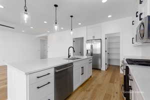 Kitchen featuring pendant lighting, stainless steel appliances, light wood-style flooring, a kitchen island with sink, and a sink