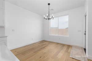 Unfurnished dining area with a notable chandelier, light wood-type flooring, visible vents, and baseboards