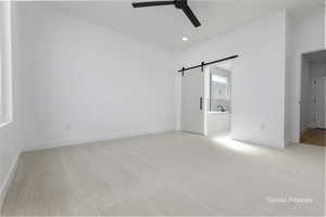 Unfurnished bedroom with light carpet, a barn door, baseboards, ensuite bathroom, and recessed lighting