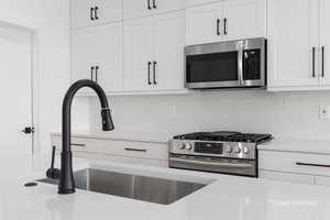 Kitchen with tasteful backsplash, white cabinetry, stainless steel appliances, and light countertops