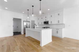 Kitchen featuring stainless steel appliances, light countertops, decorative backsplash, white cabinetry, and light wood-type flooring