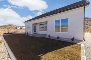 Rear view of property featuring a mountain view, a patio area, a lawn, and stucco siding