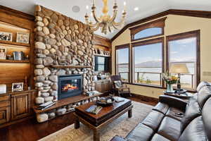 Living room featuring vaulted ceiling, a stone fireplace, wood finished floors, and a notable chandelier