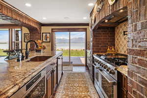 Kitchen with light stone counters, custom range hood, a water and mountain view, appliances with stainless steel finishes, and a sink