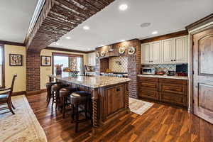 Kitchen with a kitchen island with sink, a sink, tasteful backsplash, dark wood finished floors, and crown molding