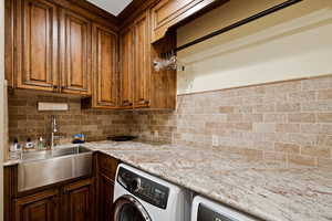 Laundry Room with washer / dryer, light stone counters, brown cabinets, and a sink