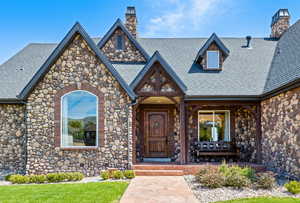 Entrance to property featuring covered porch, roof with shingles, and a chimney