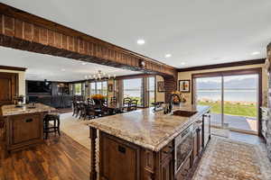 Kitchen with a breakfast bar area, dark wood-style flooring, a water view, a sink, and an island with sink