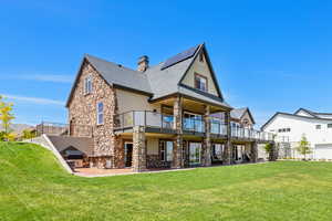 Rear view of house featuring stone siding, a chimney, a yard, a patio area, and stucco siding