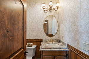 Half bathroom featuring vanity, toilet, and wallpapered walls