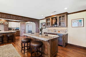 Kitchen featuring visible vents, ornamental molding, glass insert cabinets, a kitchen island, and a kitchen bar