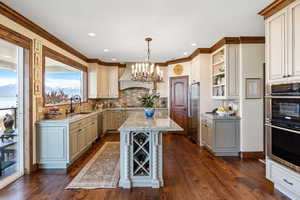 Kitchen with dark wood finished floors, custom range hood, stainless steel appliances, open shelves, and a sink