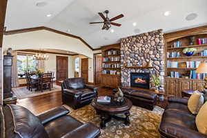 Living room with arched walkways, lofted ceiling, wood-type flooring, crown molding, and a stone fireplace