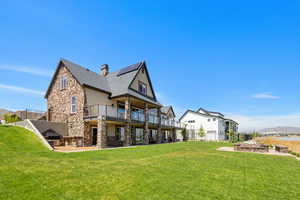 Rear view of property featuring a chimney, stone siding, a yard, and a balcony