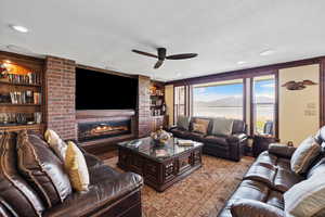 Living area with a textured ceiling, built in shelves, a brick fireplace, and a ceiling fan