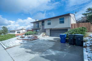 Bi-level home with a garage, concrete driveway, a chimney, fence, and brick siding