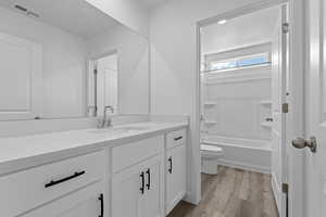 Bathroom with shower / bath combination, visible vents, toilet, vanity, and wood finished floors