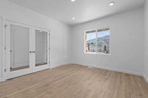 Spare room featuring a textured ceiling, recessed lighting, baseboards, french doors, and light wood-type flooring