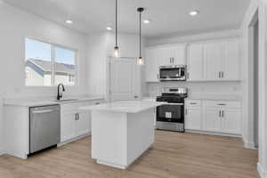 Kitchen featuring light wood finished floors, white cabinets, stainless steel appliances, light countertops, and a sink