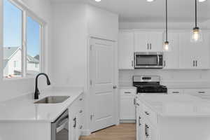 Kitchen with light wood finished floors, light countertops, appliances with stainless steel finishes, white cabinetry, and a sink