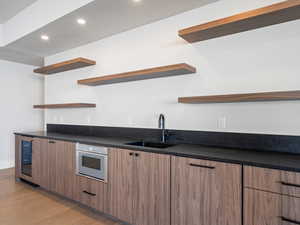 Kitchen featuring light wood finished floors, dark countertops, white oven, open shelves, and a sink