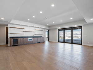 Unfurnished living room with wine cooler, a tray ceiling, indoor wet bar, visible vents, and light wood-type flooring