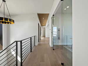 Hall with an upstairs landing, baseboards, wood finished floors, and recessed lighting