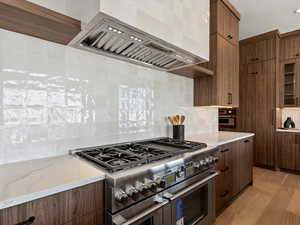 Kitchen featuring range with two ovens, custom exhaust hood, tasteful backsplash, light wood-style flooring, and light stone countertops