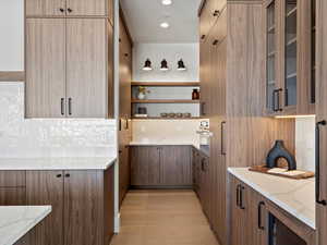 Kitchen with glass insert cabinets, tasteful backsplash, and light stone counters