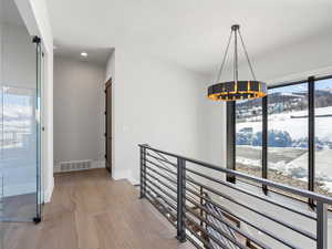 Hall featuring a notable chandelier, visible vents, an upstairs landing, wood finished floors, and baseboards