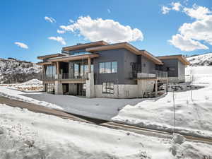 Snow covered house featuring stone siding and a balcony