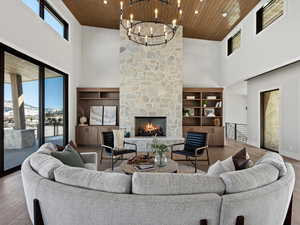 Living room with a towering ceiling, a stone fireplace, wood finished floors, wooden ceiling, and baseboards