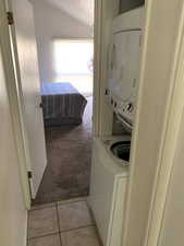 Clothes washing area featuring light carpet, stacked washer and dryer, light tile patterned floors, laundry area