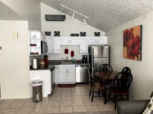 Kitchen with dark countertops, lofted ceiling, appliances with stainless steel finishes, and white cabinetry