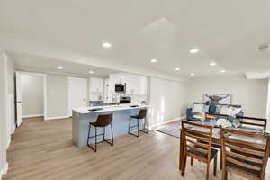 Basement kitchen living space featuring quartz countertops, stainless steel appliances, light wood-style flooring, and white cabinetry