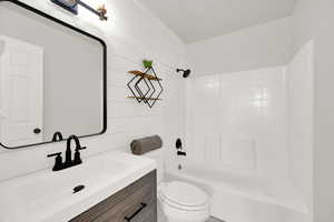 Full bathroom featuring shiplap wall, vanity, toilet, and shower / bathtub combination