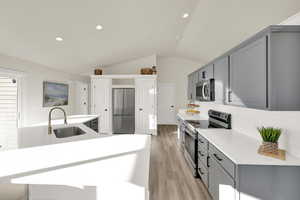 Kitchen with appliances with stainless steel finishes, light wood-style floors, gray cabinets, and a sink