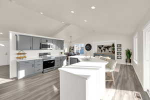 Kitchen featuring gray cabinets, light countertops, appliances with stainless steel finishes, a sink, and vaulted ceiling